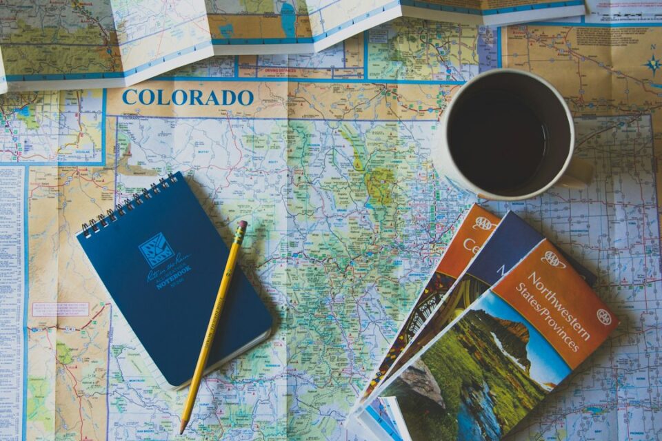 slow travel itinerary planning cover with maps, a journal, and a coffee cup on a wooden table